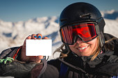Winter sports girl holding a ski pass and smiling. A concept illustrating the entry fee for skiing. Happy woman showing blank lift pass