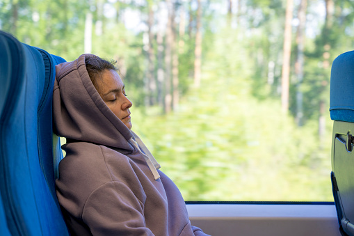 a pretty middle-aged woman sleeps sitting in a commuter train chair on her way to work. Travel, trips by train. A tired passenger in a hoodie and hood