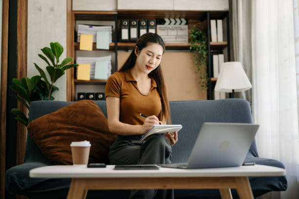 istock Asian businesswoman working in home office with working notepad, tablet and laptop documents  on sofa in living room 1495053022
