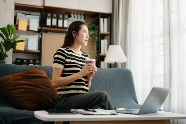 istock Asian businesswoman working in home office with working notepad, tablet and laptop documents  on sofa in living room 1495053110