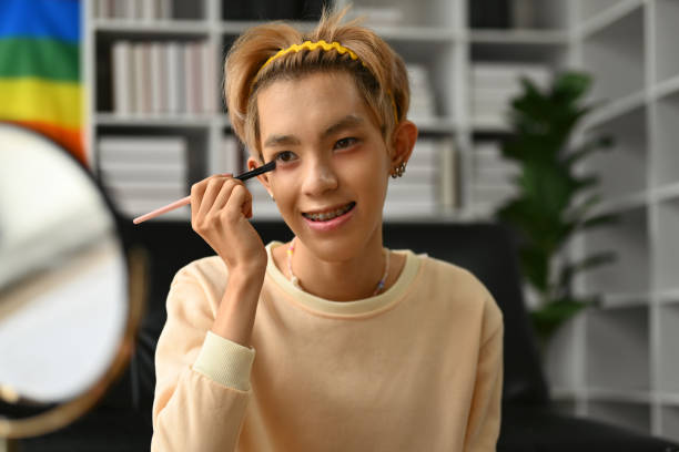 istock Pretty gay man beauty blogger applying make while streaming online video tutorial at home studio. LGBTQ, blogging and makeup. 1495055464