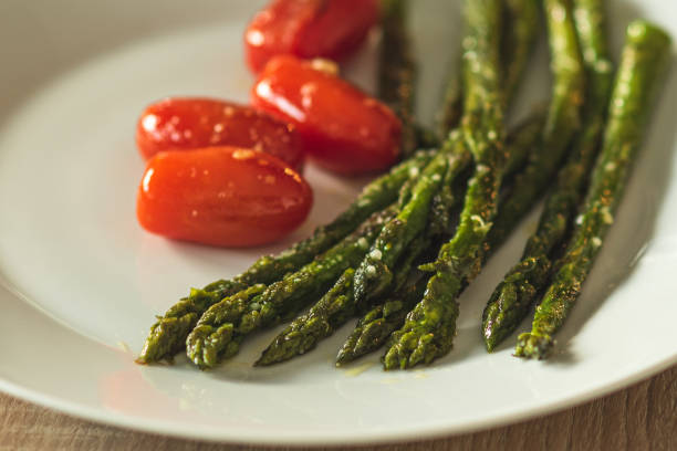 istock Cooked green asparagus and cherry tomatoes on a white plate. 1495077743