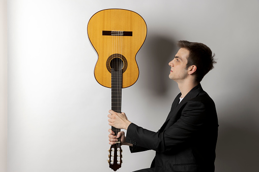 Young boy holds his guitar upside down and looks at it intently. White background