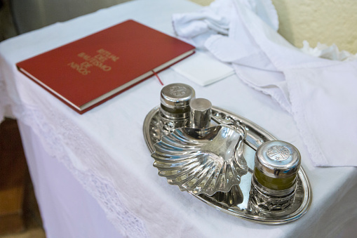 Baptism liturgical objects ready on table at church. Book, manuterge, shell, oil jugs
