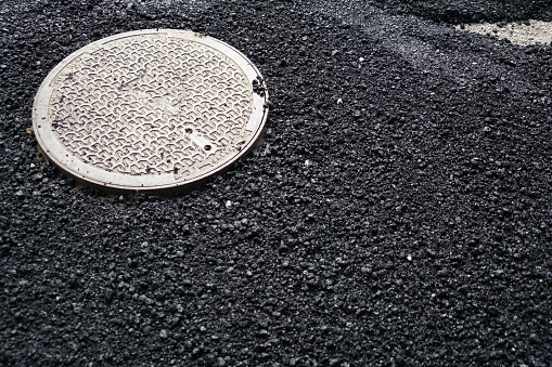 Installation of a sewer cover in the newly reconstructed road. Cover is surrounded with newly laid asphalt in Ljubljana, Slovenia, Europe.