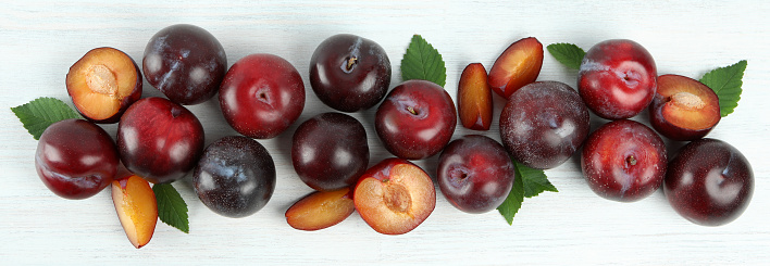 Flat lay composition with plums on white wooden background.