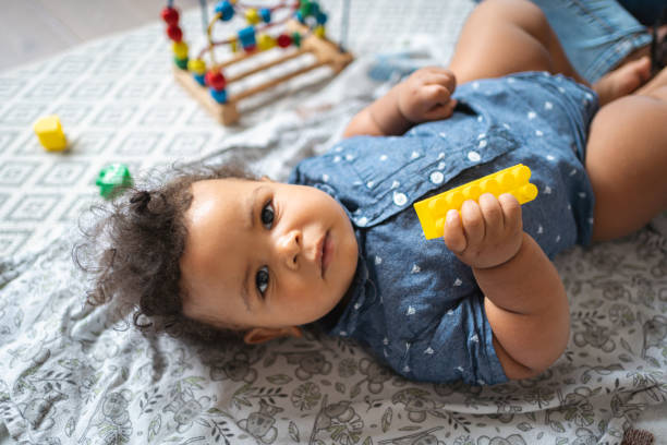 istock Mixed-race baby boy looking at camera, while lying on the blanket with a toy in his hand 1495085179