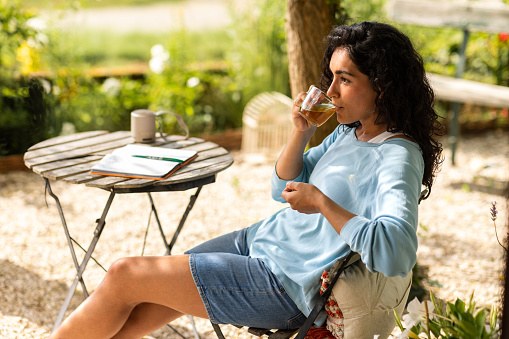 A side view of a young woman who is on a self care trip to a house in Toulouse in the south of France. She is sitting with her journal and a cup of tea and having a mindful moment to herself before dinner.