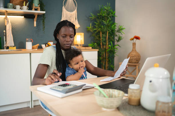 While her son sitting in her lap, worried woman Black ethnicity doing her home finances stock photo