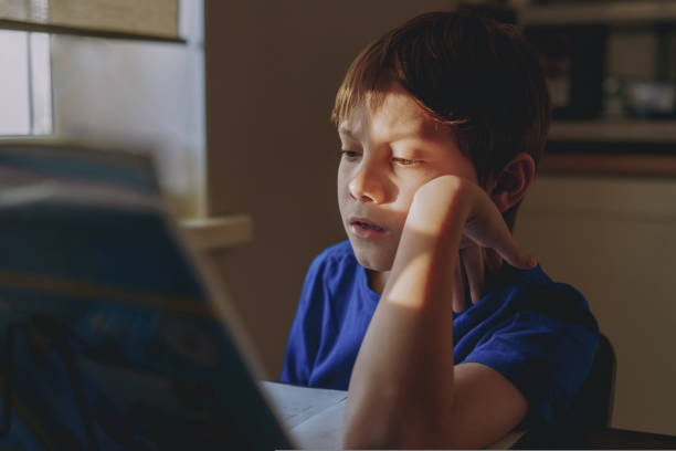 istock stressed tired boy doing homework at home at the desk by the window. 1495087679