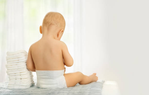 baby from back sitting in diaper next piles of diapers