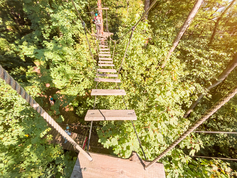 Rope park in wood forest.High-altitude climbing training on adventure track, equipped with safety straps and protective helmet.Adventure park close-up. Summer fun and sports for adventurous people.