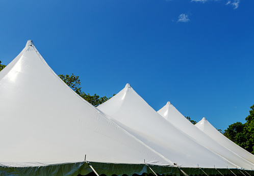 Canopy of large white event tent with four peaks held up by poles, under a deep blue sky.