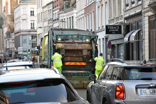 Refuse Collectors Hanging On Garbage Truck While On Duty, Building Exterior, Land Vehicle, Road Traffic, Retail Store Scene In Lille France Europe