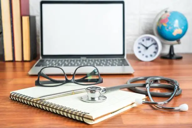 A modern workstation with a laptop, a notebook and a stethoscope