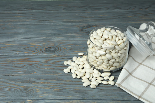 Jar with white beans on gray wooden background.