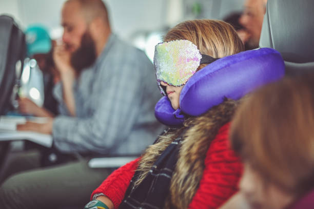 Girl uses a neck pillow and eye mask to sleep while traveling on an airplane stock photo