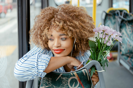 Attractive African American Woman With Headphones and Flowers Commuting by Public Transport. Public Transport Concept