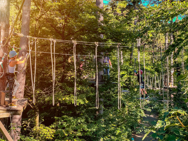 Summer fun and sports for adventurous people.Rope park in wood forest.A people walks a rope bridge between trees in an amusement park in safety gear and a helmet. High-altitude climbing training on adventure track, equipped with safety straps and protective helmet.Adventure park close-up. diversión de verano y deportes para personas aventureras. primer plano del parque de aventuras. parque de cuerdas en bosque de madera. un pueblo camina por un puente de cuerda entre los árboles en un parque de diversiones con equipo de seguridad y un cas