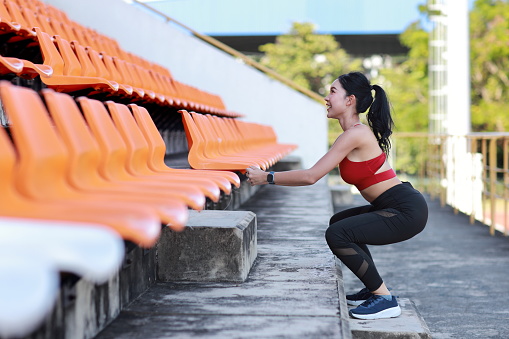 Strong and beautiful asian fitness female sportswoman doing squat exercise and workout at stadium while akimbo and looking away