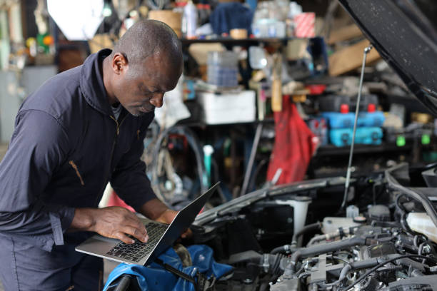 istock Man technician car mechanic in uniform checking maintenance a car service with computer at repair garage station. Car repair service concept 1495105165