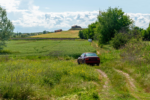 Green crops with a country house in a hilly field and parked cars around.