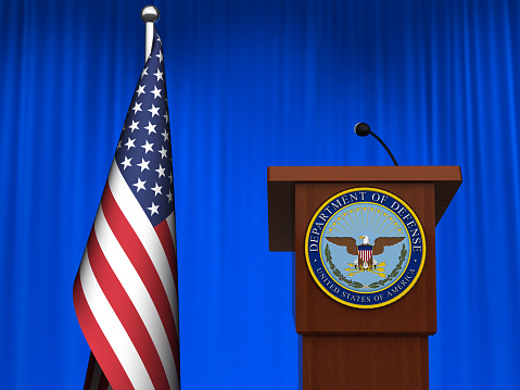 Mature adult African American politician and mid adult Hispanic male political adviser are discussing city budget during a meeting or speech in town hall. Audience members are asking questions while men stand behind podium.