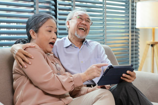 istock Happy smiling asian senior couple sitting on sofa and using tablet while online video call with friend or relative cousin at home living room. Internet information technology and lifestyle concept. 1495110325