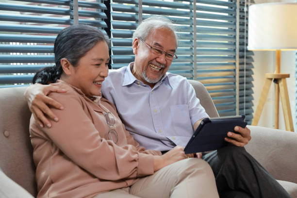 istock Happy smiling asian senior couple sitting on sofa and using tablet while online video call with friend or relative cousin at home living room. Internet information technology and lifestyle concept. 1495110336