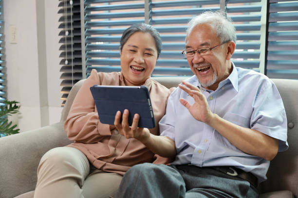 istock Happy smiling asian senior couple sitting on sofa and using tablet while online video call with friend or relative cousin at home living room. Internet information technology and lifestyle concept. 1495110431