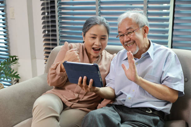 istock Happy smiling asian senior couple sitting on sofa and using tablet while online video call with friend or relative cousin at home living room. Internet information technology and lifestyle concept. 1495110485