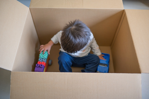 2 years old baby boy having fun playing with toy trucks inside a huge and empty delivery box in the living room at home. A toddler gleefully plays in a large delivery box, turning it into a world of imagination and endless fun