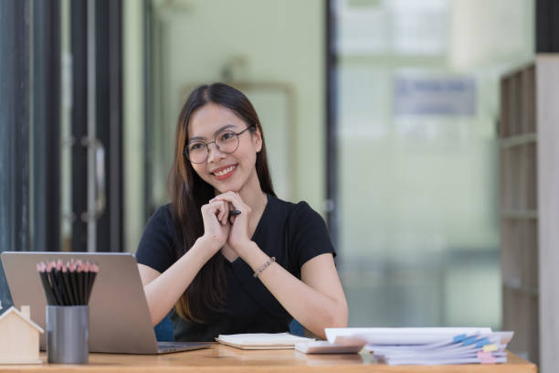 istock A beautiful young Asian businesswoman is saving and checking work and documents with her laptop computer at her desk with a bright smile on her face. 1495112227