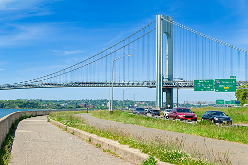 High resolution stitched image of the Verrazano-Narrows Bridge on a spring morning with Cars driving on Belt Parkway. The bridge connects boroughs of Brooklyn and Staten Island in New York City. The bridge was built in 1964 and is the largest suspension bridge in the USA. 
The photo was taken from the Shore promenade in Bay Ridge Brooklyn. Canon EOS 6D full frame censor camera. Canon EF 85mm f/1.8 USM Prime Lens. 3:2 Image Aspect Ratio.