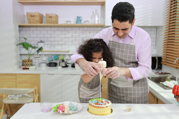istock Happy lovely asian single dad and cute daughter in apron having fun with teaching and decorating homemade cake in the kitchen. Family lifestyle cooking with education concept. 1495113473