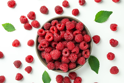 Red juicy raspberries in a bowl and raspberries with leaves on a white background.