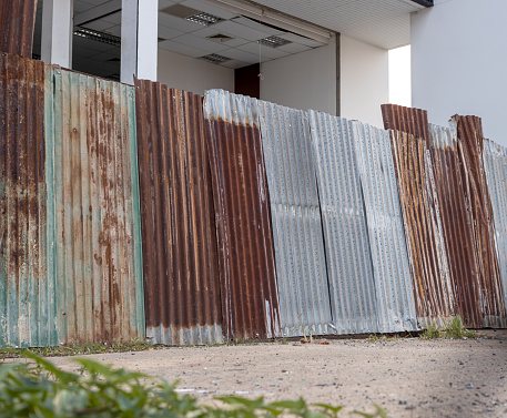 Low angle view of old galvanized sheet walls forming a wall on the ground enclosing the building for safety during construction and renovation, common in rural Thailand.