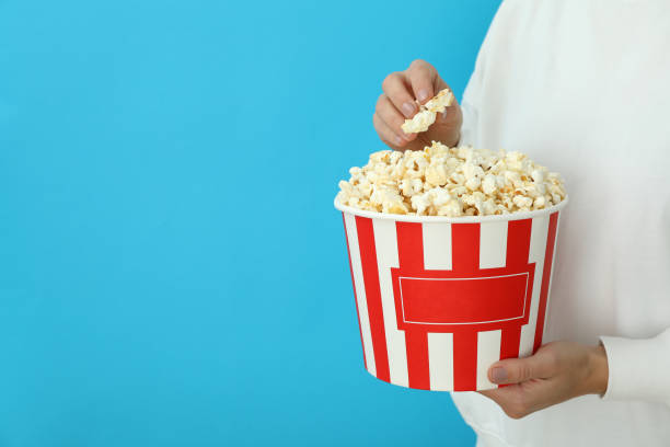 istock Woman holds paper cup with popcorn on blue background 1495122665