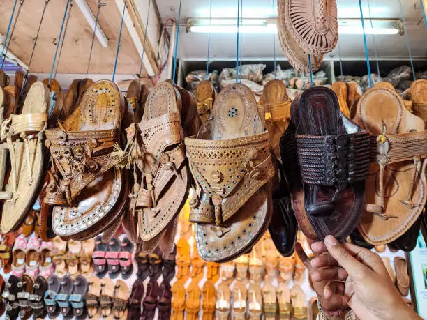 Photo of Stock photo of popular and traditional kolhapuri chappal hanging in the display for sale in the local shop.It is handmade leather chappal with unique design and color at Kolhapur, Maharashtra, India.