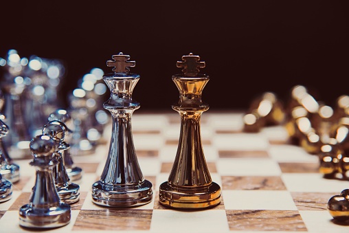 A close-up of a chess set on a wooden table, featuring two opposing sets of pieces made of metal