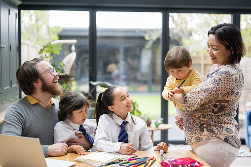 Multiracial couple in early 40s, 12-month old baby boy, and schoolgirls in uniforms aged 6 and 11 spending time together.