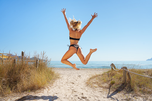 Happy young woman jumping at sand beach. Relaxing, fun, and enjoy holiday at tropical paradise beach with blue sky. Off to summer vacation.