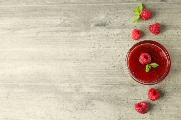 istock Glass bowl of raspberry jam with ingredients on gray textured background 1495129655