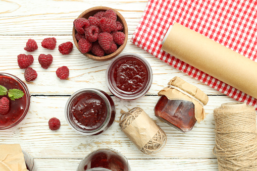 Concept of cooking raspberry jam on white wooden table.