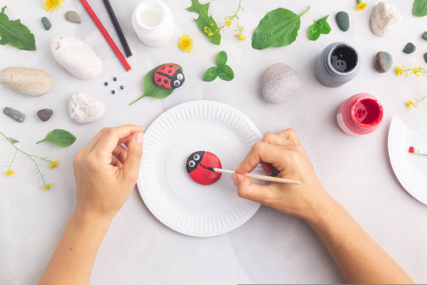 istock Drawing a ladybug on a stone with acrylic paints. Home hobbies are authentic. Artwork on stones. Woman hands. 1495132477