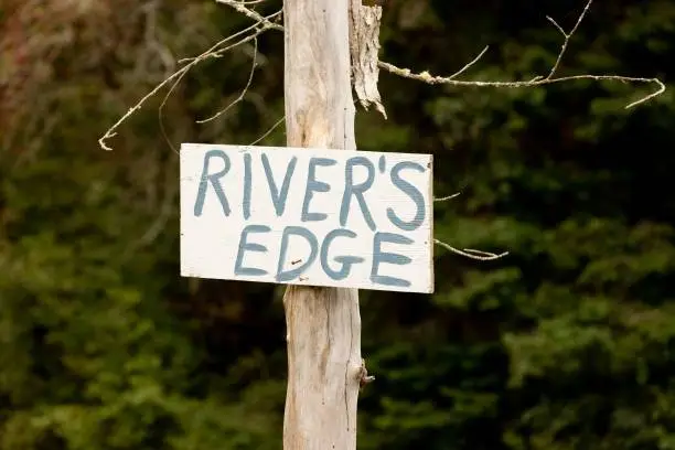 The image depicts a wooden pole with a sign attached to it, located on the edge of a river