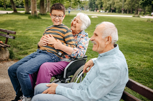 Boy spending time with his grandparents in the park having fun. Grandparent with disability supported by his grandson.