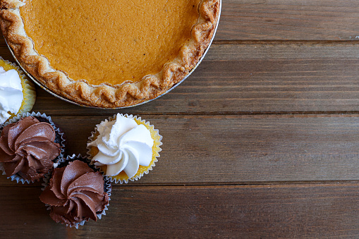 A pumpkin pie and cupcakes on a wooden table