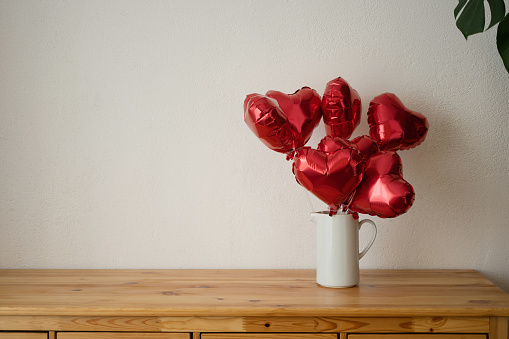 Red heart shaped balloons in vase on wooden table and white wall background. Valentine's day concept.
