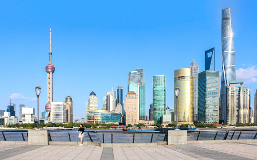 Female tourist standing against railings at Shanghai bund with the iconic Shanghai skyline view of Lujiazui behind, boat on the Huangpu River